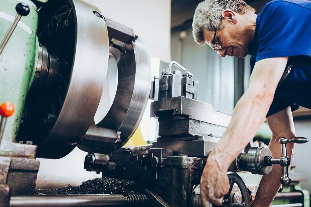 Facharbeiter mit Schutzbrille bedient eine Drehmaschine in einer Werkstatt, Blick auf das Spannfutter und den Werkzeugschlitten