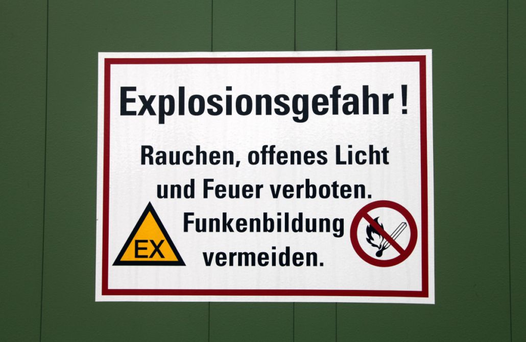 Ein Warnschild an einer grünen Wand mit der Aufschrift Explosionsgefahr! sowie Symbolen für Rauchverbot und Funkenbildung