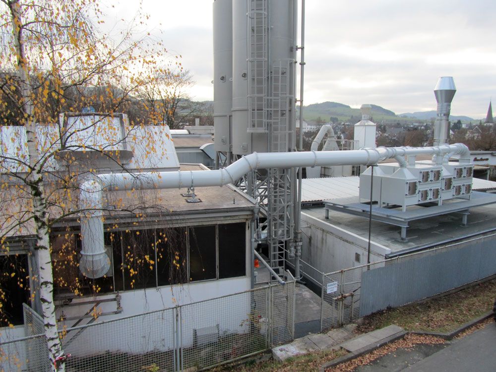 Absauganlage auf einem Gebäudedach, über weit verzweigte Rohrleitungen mit einem Silo verbunden, im Hintergrund eine Ortschaft