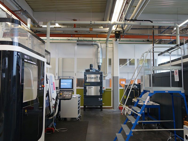 Afzuiginstallatie in een productiehal tussen CNC-machines, via leidingen in het plafond aangesloten op het afzuigsysteem