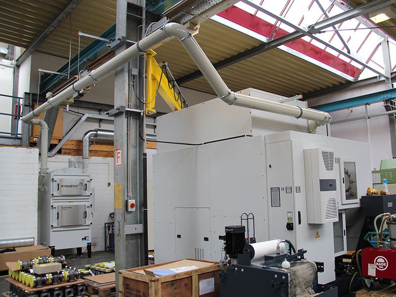 Industriehalle mit einer Absauganlage im Hintergrund, über Deckenrohrleitungen mit einer Werkzeugmaschine verbunden